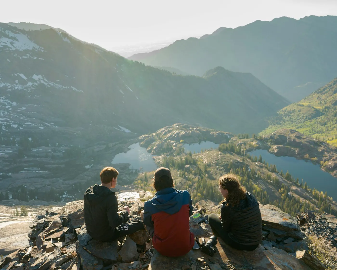 Three friends sitting on a cliff overlooking a lake and mountains